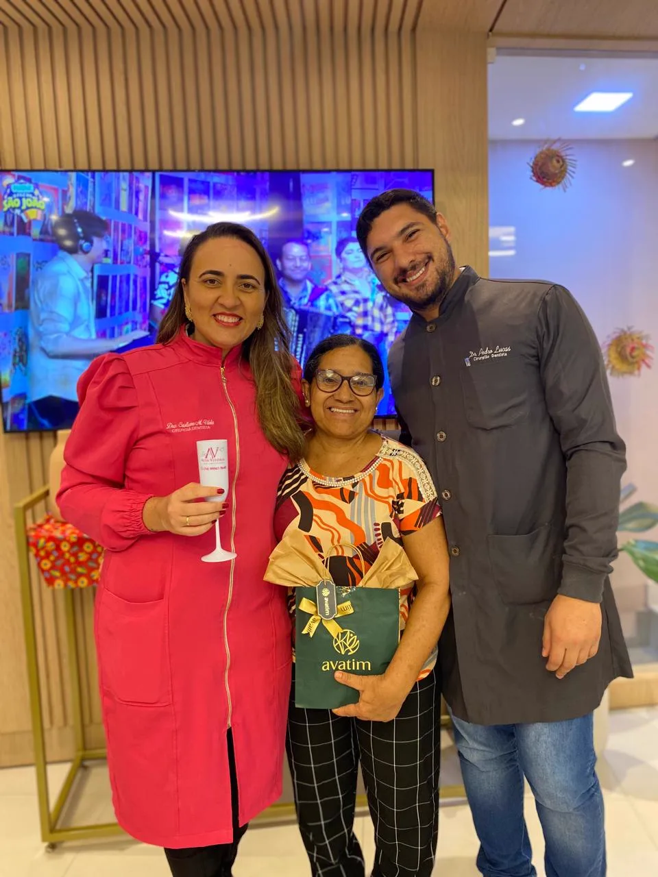 Paciente entre os dois dentistas da clínica, todos sorrindo