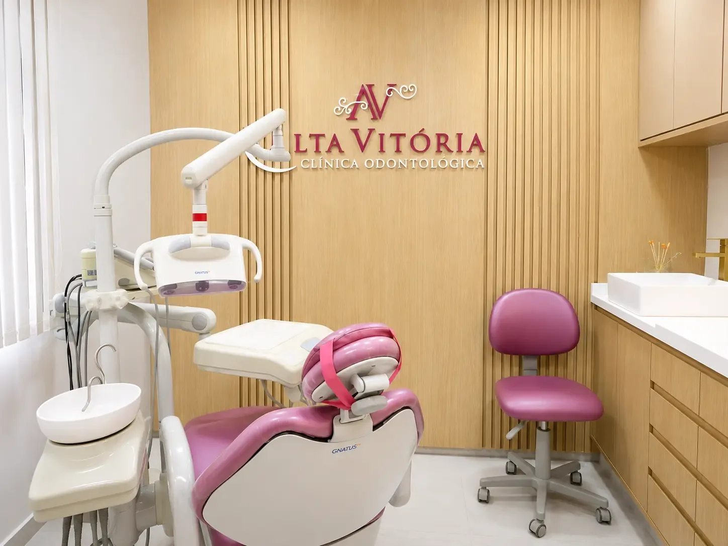 Consultório com cadeira odontológica rosa e logo da clínica